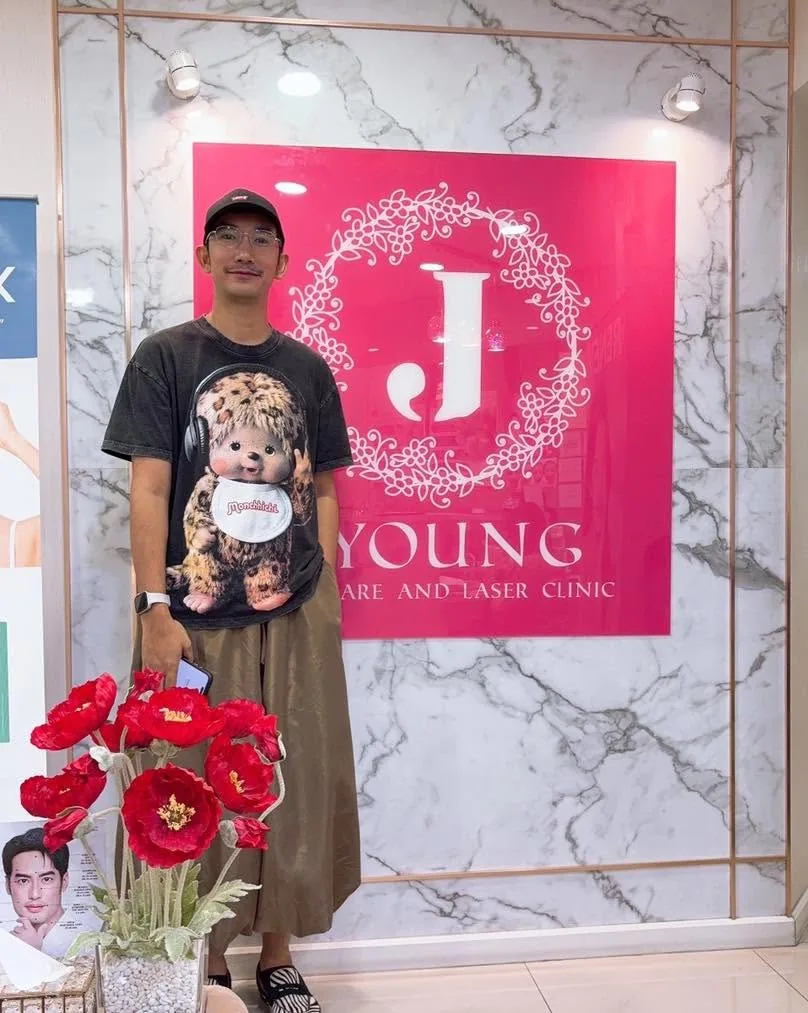 ลูกค้าถ่ายภาพที่ระลึกหน้าป้าย J Young Clinic สวมเสื้อยืดสีเข้มและหมวก