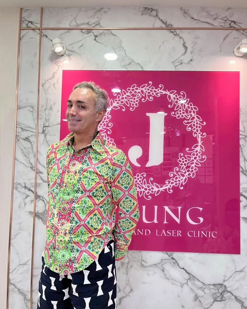 ลูกค้าถ่ายภาพที่ระลึกหน้าป้าย J Young Clinic สวมเสื้อเชิ้ตลวดลายสีสันสดใส